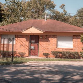 A single-story brick house with a red roof and a small front yard.