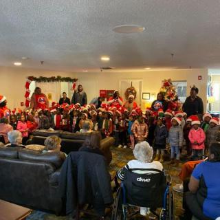 Children perform a holiday program for seniors in a festive setting.