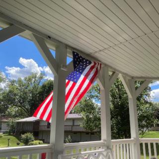 A vibrant American flag gently waving on a sunny day from a porch.