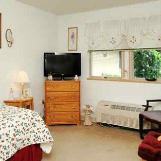 A cozy bedroom with a television, dresser, and bedspread.