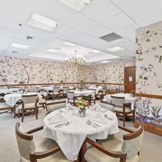 An elegant dining room with floral wallpaper, chandeliers, and neatly set tables.