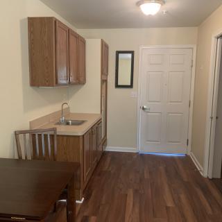 A small kitchen area with wooden cabinets, a sink, and a dining table set on a wooden floor.