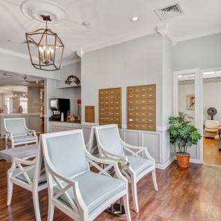 A modern waiting area featuring comfortable chairs, wooden flooring, decorative lighting, and wall-mounted mailboxes.