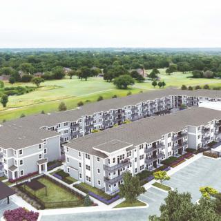 An aerial view of a modern apartment complex with surrounding greenery and a parking lot.