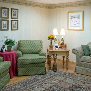 A cozy living room with green patterned armchairs and a sofa, featuring a small wooden table with lamps and decor pieces.