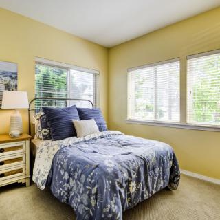 A cozy bedroom with a neatly made bed and ample natural light from multiple windows.