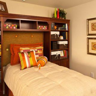 A cozy bedroom with a single bed and wooden shelves adorned with decorative orange pillows and wall art.