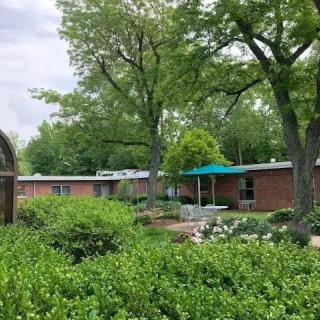 A tranquil garden setting with lush greenery and a brick building in the background.