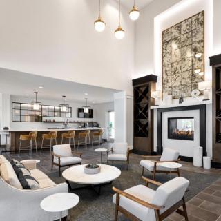 A modern living room with an open seating area, featuring a high ceiling, chandelier lighting, and a stylish bar counter.