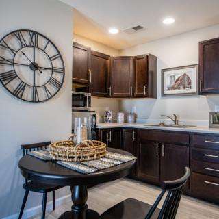 A modern kitchen with dark cabinets and a small dining area featuring a large wall clock.