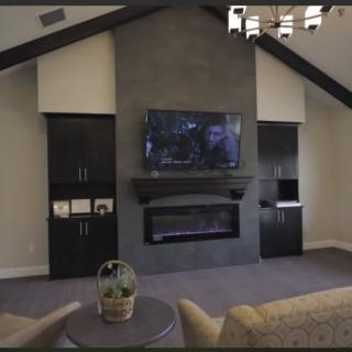 A modern living room with a vaulted ceiling, featuring a large television mounted above a sleek fireplace and surrounded by dark cabinetry.