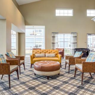 A spacious living room with a yellow sofa, armchairs, and a large ottoman, featuring ample natural light from large windows.