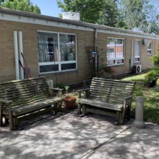 Outdoor seating area with wooden benches and a brick building in the background.
