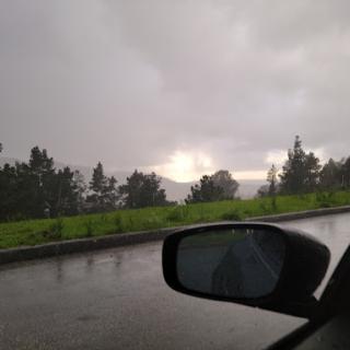 A view of a stormy sky with rain falling along the roadside.