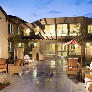 A cozy courtyard with outdoor seating in front of a well-lit residential building during the evening.