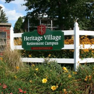 Sign for Heritage Village Retirement Campus surrounded by flowers and greenery.