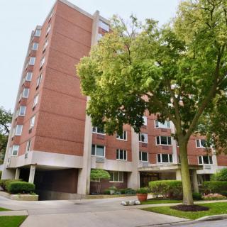 A brick apartment building surrounded by trees in an urban setting.