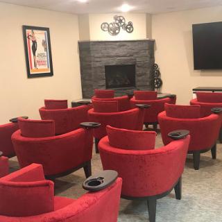 A cozy home theater setup with red chairs facing a large screen and fireplace.