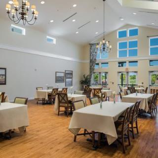 A spacious dining room with elegant chandeliers, large windows, and neatly arranged tables.