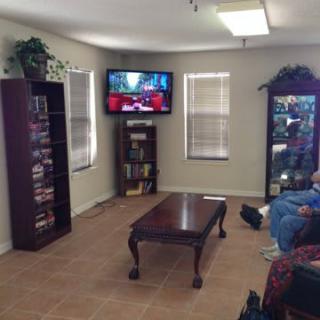 A cozy living room with a wall-mounted television, bookshelf, and comfortable seating.
