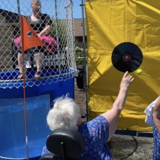 A lively outdoor event featuring a dunk tank, where participants aim to hit the target and splash the person sitting above.