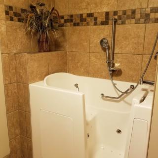 A walk-in bathtub with a door and handheld showerhead in a tiled bathroom.