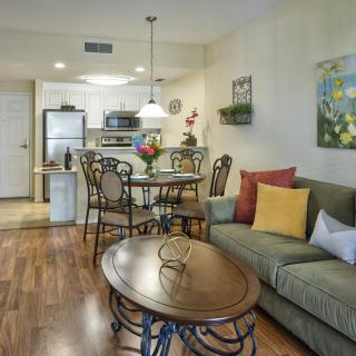 A cozy living and dining area with a view into the kitchen, featuring a sofa, an oval coffee table, and a dining set with decorative cushions.
