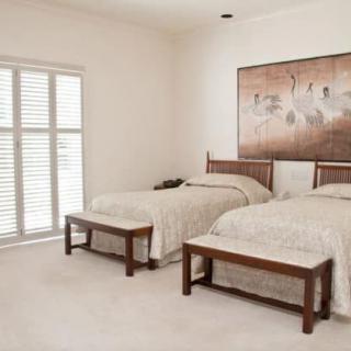 A neatly arranged bedroom featuring twin beds with a central painting and window blinds.