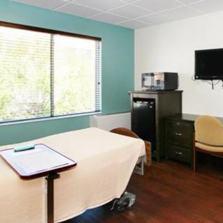 A small medical examination room with a bed, television, and large window.