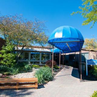 The entrance of a building with a blue canopy and landscaped surroundings.