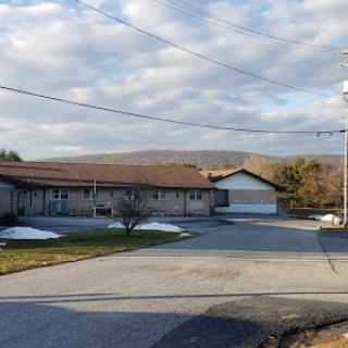 A peaceful view of a residential building with a backdrop of rolling hills and cloudy sky.