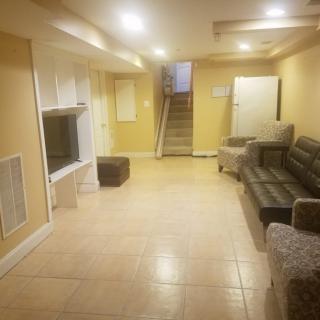 A spacious basement living area with a sofa, television, and tiled flooring.