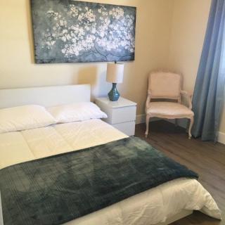 A cozy bedroom with a neatly made bed, a blue throw blanket, and decorative artwork above the headboard.