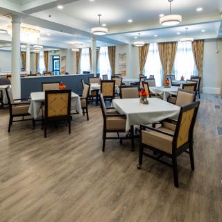 A well-lit dining area with neatly arranged tables and chairs, featuring elegant curtains and a wooden floor.