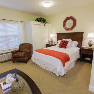 A cozy bedroom with a neatly arranged bed, an armchair, and decorative elements.
