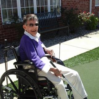 An elderly person in a wheelchair enjoys a sunny day outdoors.