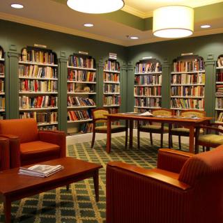 A cozy library reading room with bookshelves, comfortable chairs, and tables.