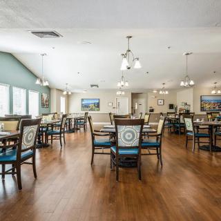 A spacious dining room with arranged tables and chairs, wood flooring, and ceiling lights.