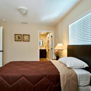 A cozy bedroom with a neatly made bed, bedside lamp, and a window letting in natural light.