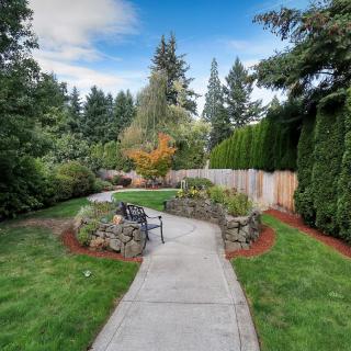 A scenic garden pathway with a bench surrounded by lush greenery and trees.