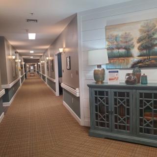 A well-lit corridor with decorative elements and artwork on the walls, featuring a carpeted floor and a console table.