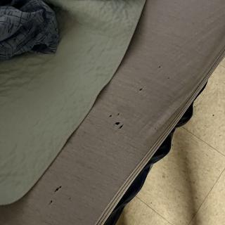 A bedsheet with multiple holes lies on a bed beside a tiled floor.