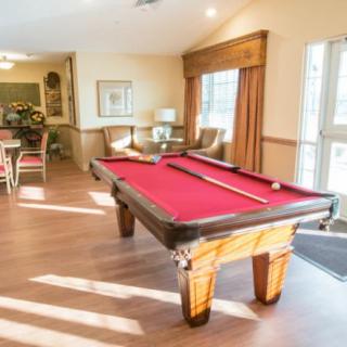 A sunlit game room featuring a red-felt pool table and seating area.