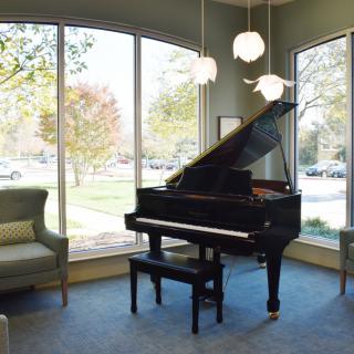 A grand piano elegantly placed in a sunlit living room with large windows and comfortable seating.