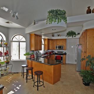 A modern kitchen featuring wooden cabinets, a central island with bar stools, and stainless steel appliances, enhanced by natural light and greenery.
