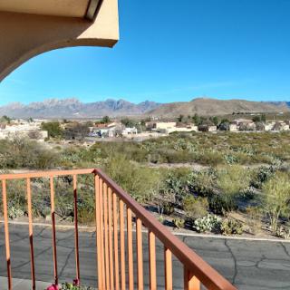 A serene view from the balcony overlooking desert vegetation and distant mountains under a clear blue sky.