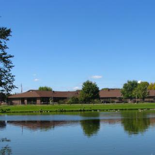 A serene view of a building reflected on calm waters, with a clear blue sky above.
