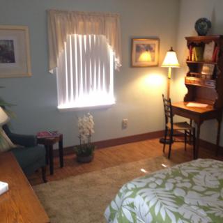 A cozy and well-lit bedroom featuring a wooden desk, chair, and a lamp near a window with curtains.
