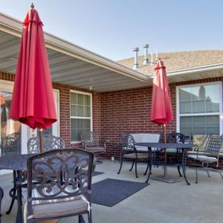 A cozy patio area with red umbrellas and metal furniture against a brick building backdrop.