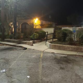 A dimly lit parking lot at night, featuring a pathway leading towards a landscaped area.